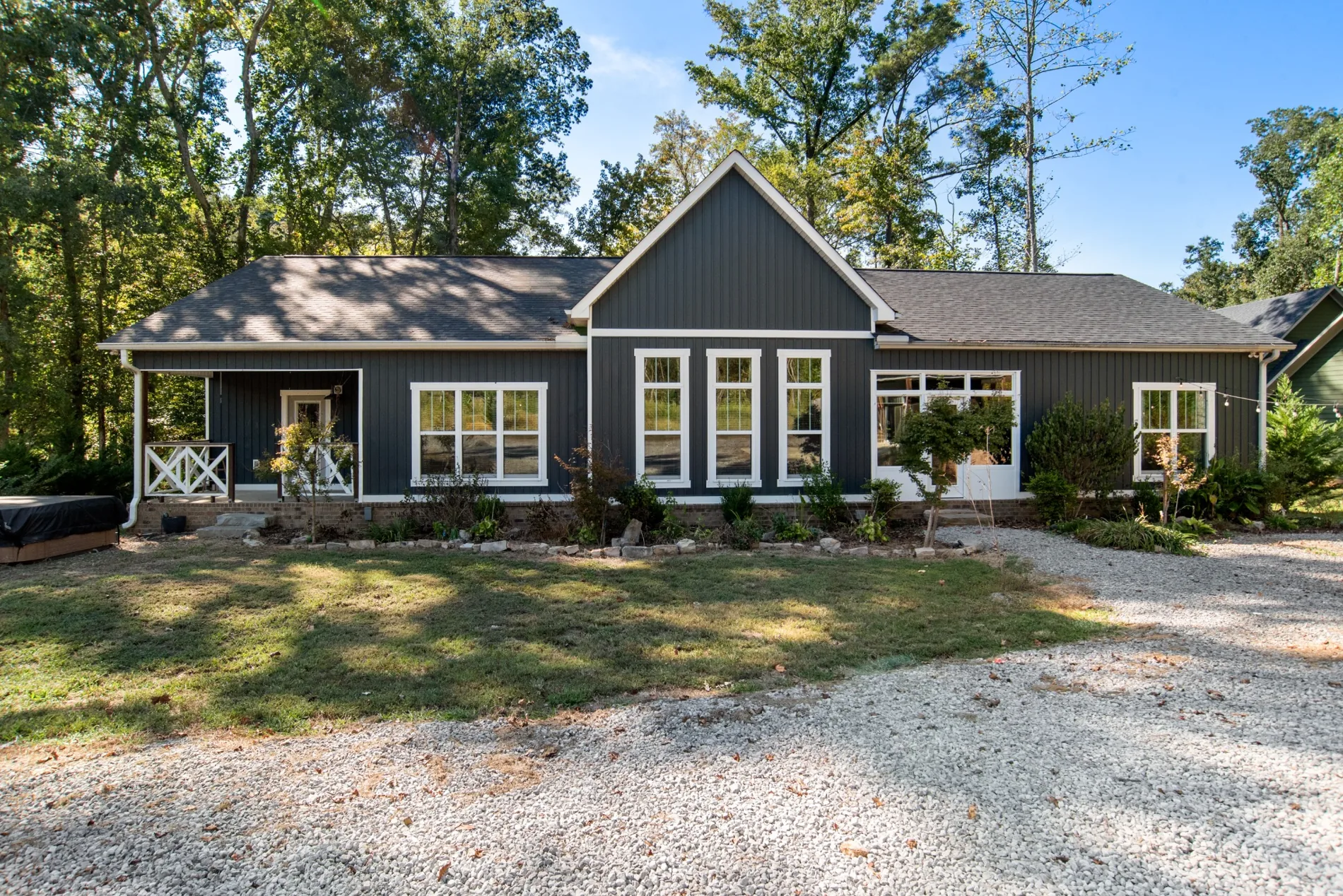 Front exterior of charcoal-gray house with white trim and wooded surroundings